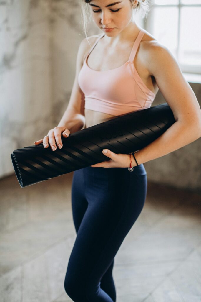 Fit woman in a yoga studio holding a black yoga mat, ready for a workout.